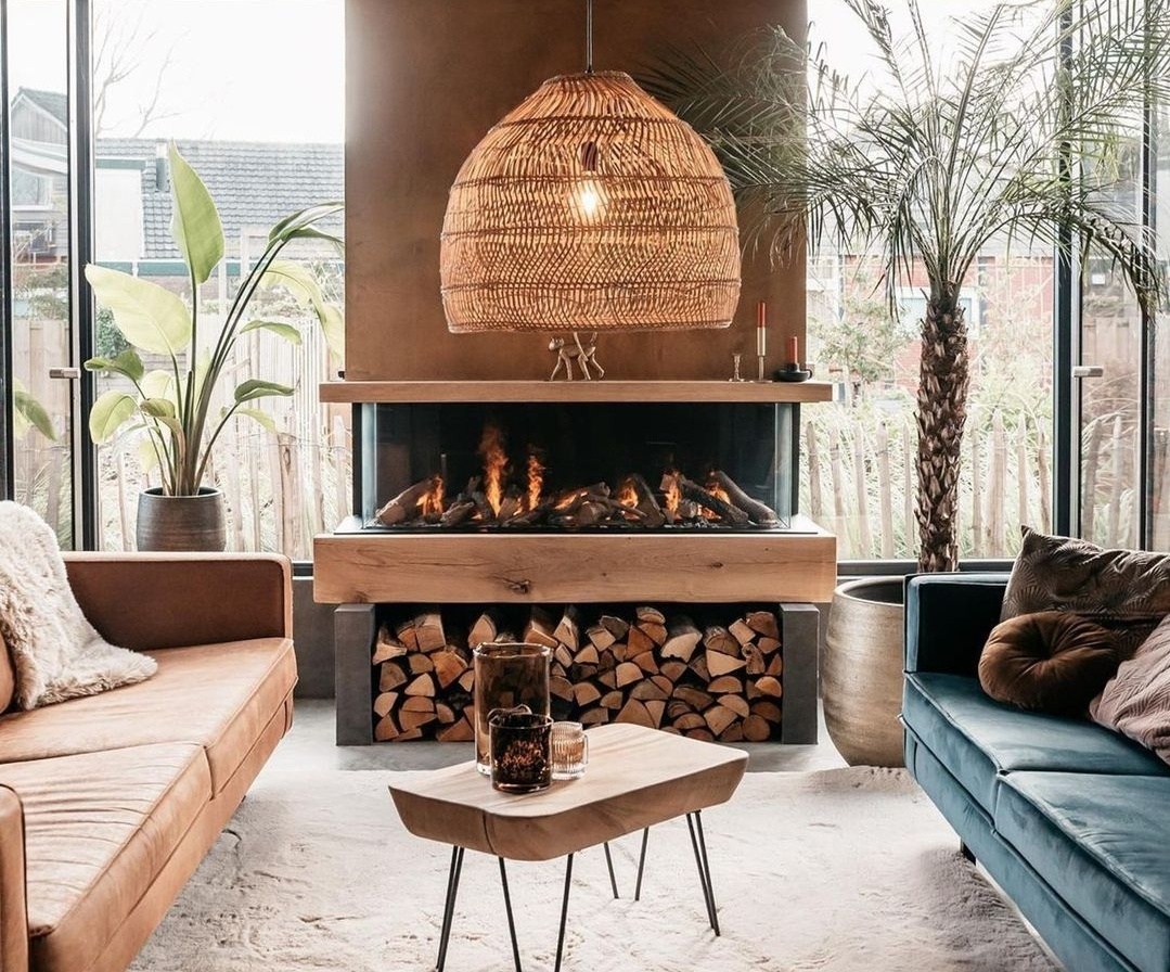 Sala de estar moderna con chimenea de leña, sofá marrón, sofá azul, mesa de madera y lámpara colgante de mimbre.